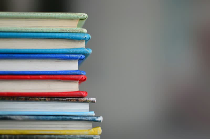 A colourful stack of closed hardcover books on a plain background.